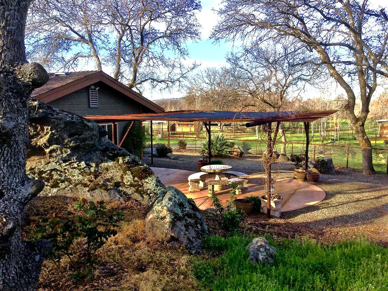 Une maison de campagne dotée d’un patio agrémenté d’une pergola, de coins salon extérieurs et d’une fontaine en pierre.