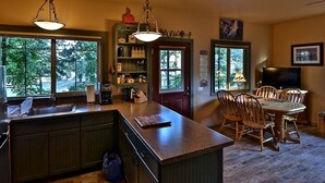 A kitchen with a large island, wooden cabinets, and a dining area with a table and chairs. - Quiet Cottage Rental for Two in Horse Country near Yosemite National Park Gateway, California (Catheys Valley)