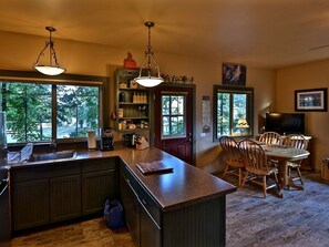 A kitchen with a large island, wooden cabinets, and a dining area with a table and chairs. - Quiet Cottage Rental for Two in Horse Country near Yosemite National Park Gateway, California (Catheys Valley)