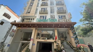 Un hotel con un cartello che recita 'Diamond Beach Hotel', una scala che conduce all'ingresso e una statua nei pressi dell'entrata.