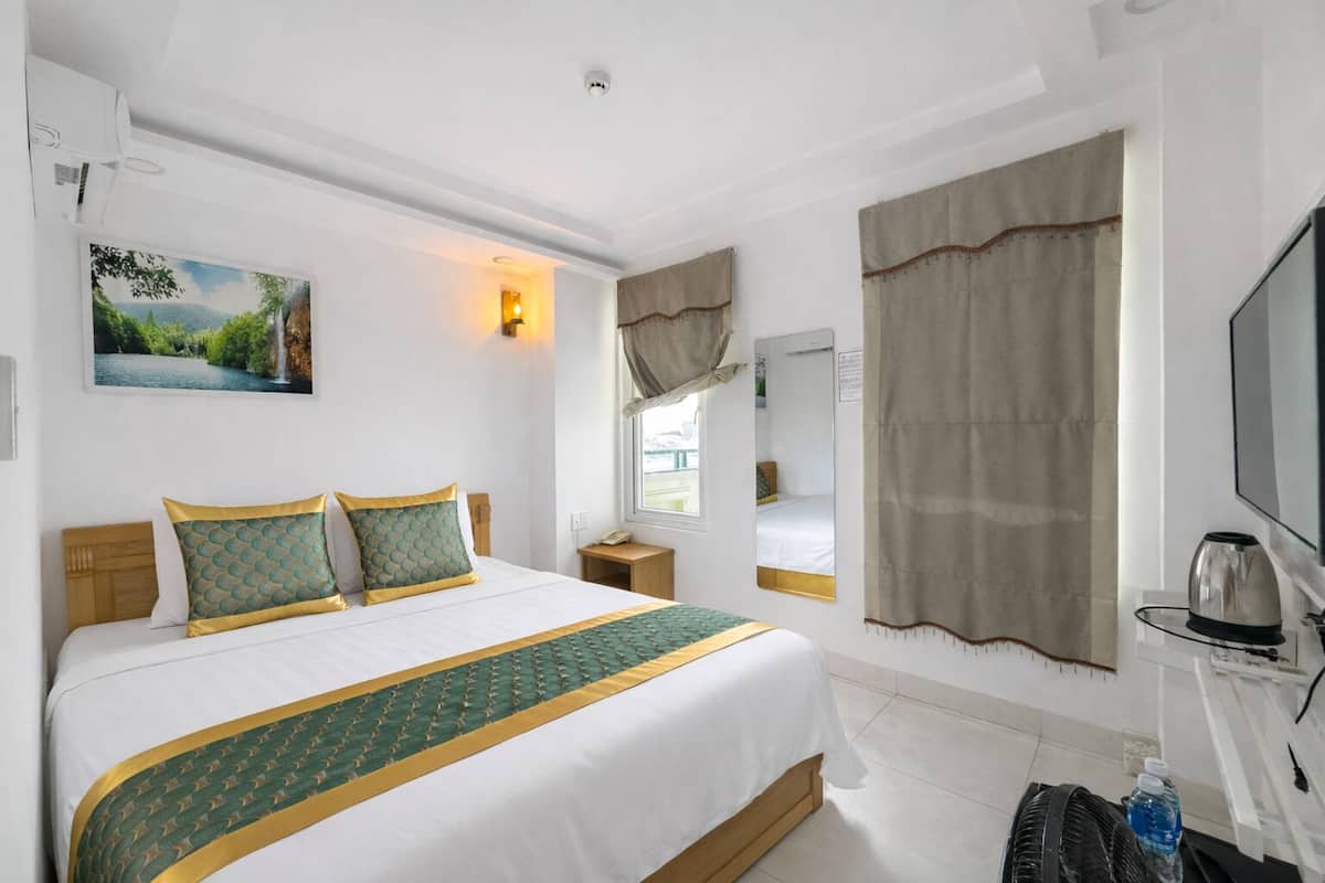 A hotel room with a bed, a bedside table, a mirror, a window with curtains, and a television.
