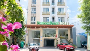 Un hotel a più piani con un balcone ad ogni piano, un ingresso ben visibile e un'area di parcheggio con auto.