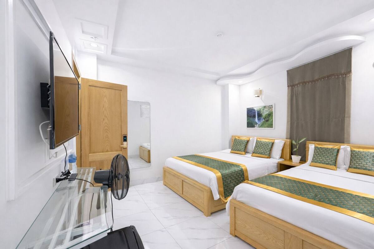 A hotel room with two beds, a TV, a desk with a fan, and a window with curtains.