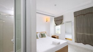 Una camera d'albergo con un letto, comodino, finestra con tende e zona doccia.