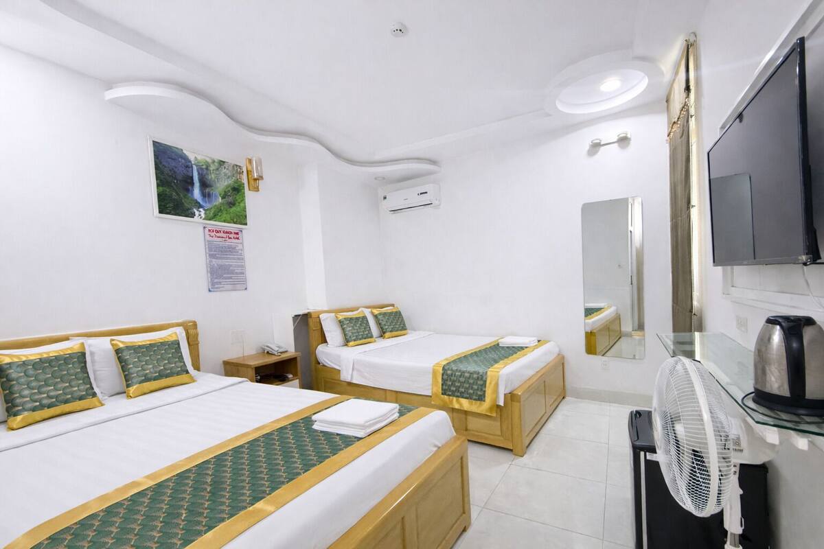 A hotel room with two single beds, a TV, a fan, and a mirror.