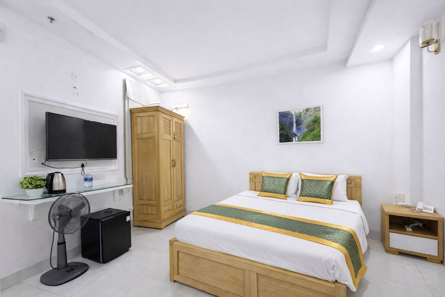Quarto com cama, televisão, guarda-roupa, mesa de cabeceira e um quadro na parede.