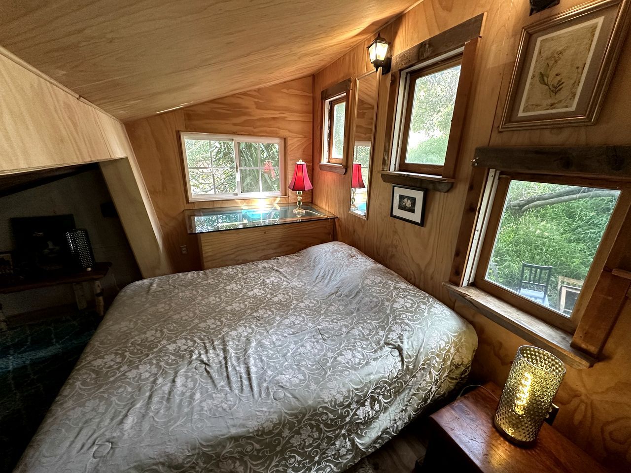 Un dormitorio con cama, escritorio y ventana con vistas a la vegetación.