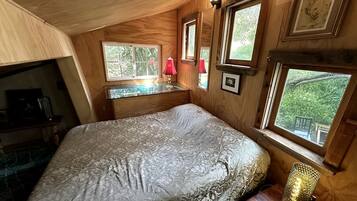 Un dormitorio con cama, escritorio y ventana con vistas a la vegetación.