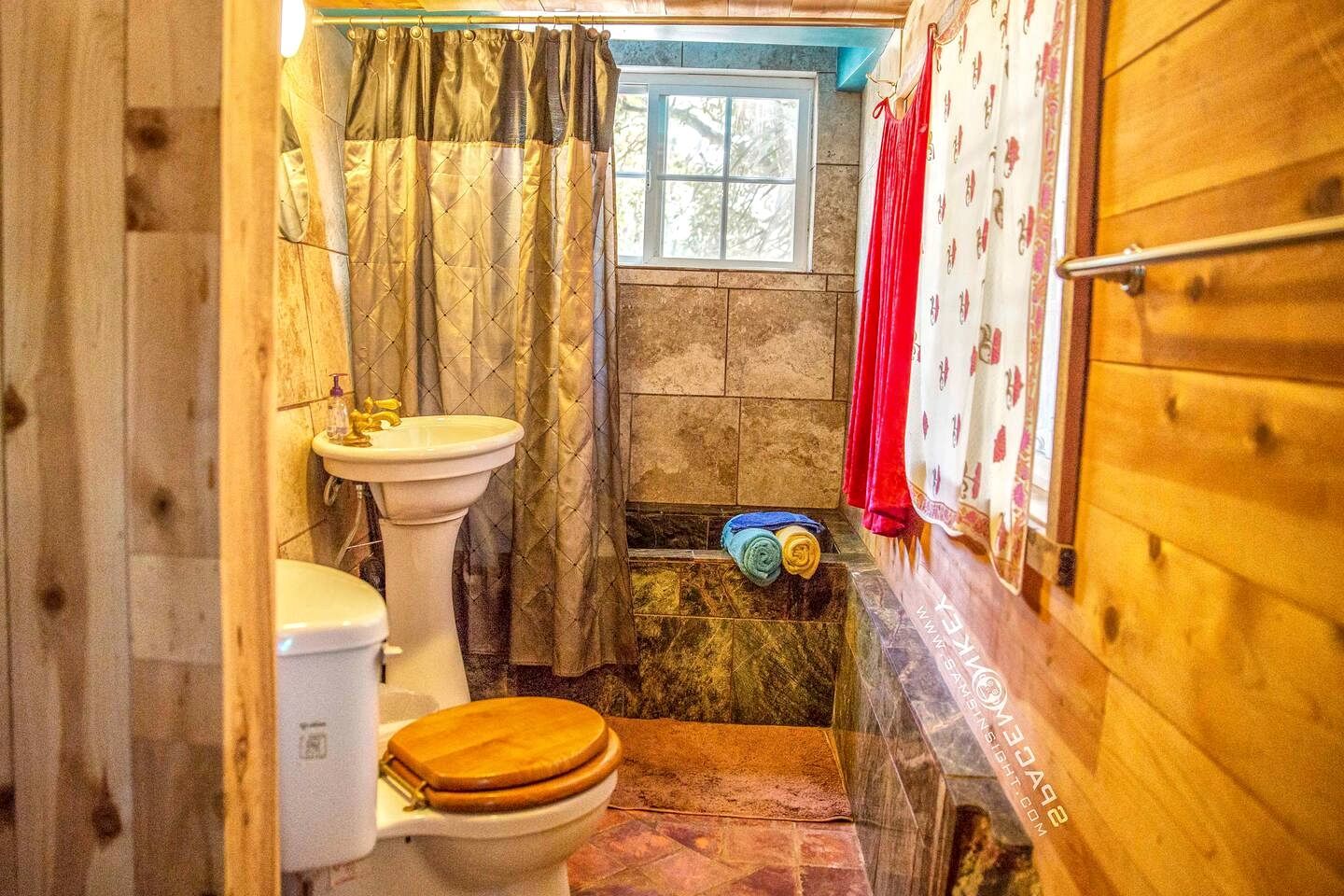 Ein kleines Badezimmer mit Holzboden, Toilette, Waschbecken und Fenster.