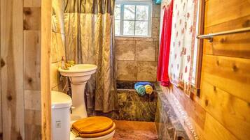 Ein kleines Badezimmer mit Holzboden, Toilette, Waschbecken und Fenster.