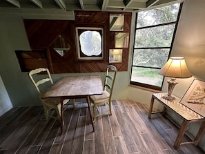 A dining area with a wooden table and chairs, a window with a view of greenery, and a lamp on a side table. - Cozy Unique Cottage for a Peaceful Escape in Nature in Topanga, California (Topanga)