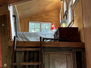 Une chambre à coucher aménagée dans un espace ouvert, avec un lit superposé, des murs en bois, une fenêtre et une lampe rouge.