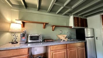 A compact kitchen with a microwave, toaster, and coffee maker on the counter, wooden cabinets, and a refrigerator.