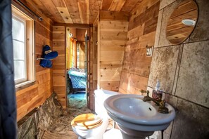 A wooden cabin bathroom with a toilet, sink, and a window.