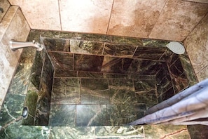 A bathroom with a tiled floor, a shower area, and a handrail.