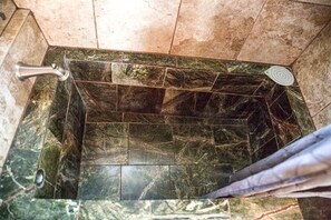 Un baño con suelo de baldosas, zona de ducha y barra de apoyo.