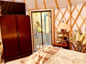 Habitación con carpa, una cama, un armario de madera, un escritorio con lámpara y vistas a través de una puerta.