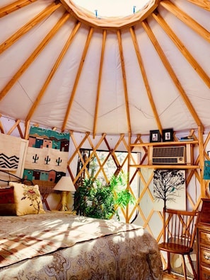 Interieur van een joert met een bed, een stoel en diverse wanddecoraties.