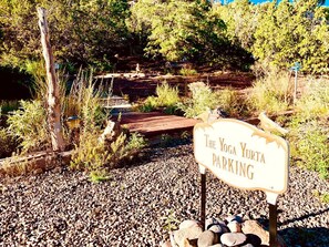 Un panneau indiquant le «parking du Yoga Yurt», situé dans un cadre naturel avec un sol de gravier et des structures en bois.