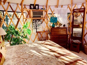 Una habitación tipo tienda de campaña acogedora y bien iluminada, con una cama, muebles de madera y una planta grande.