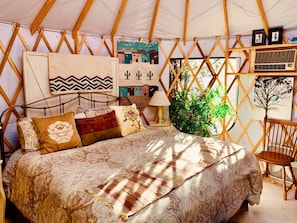 Een gezellige, goed verlichte tentkamer met een bed, kussens, een lamp en een plant.
