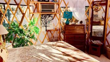 A cozy, well-lit tent-style room with a bed, wooden furniture, and a large plant.