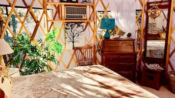 Une pièce confortable, de style tente, bien éclairée, avec un lit, des meubles en bois et une grande plante.