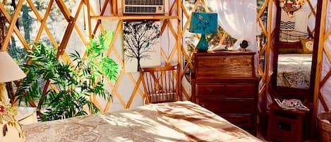 Een gezellige, goed verlichte tentkamer met een bed, houten meubels en een grote plant.