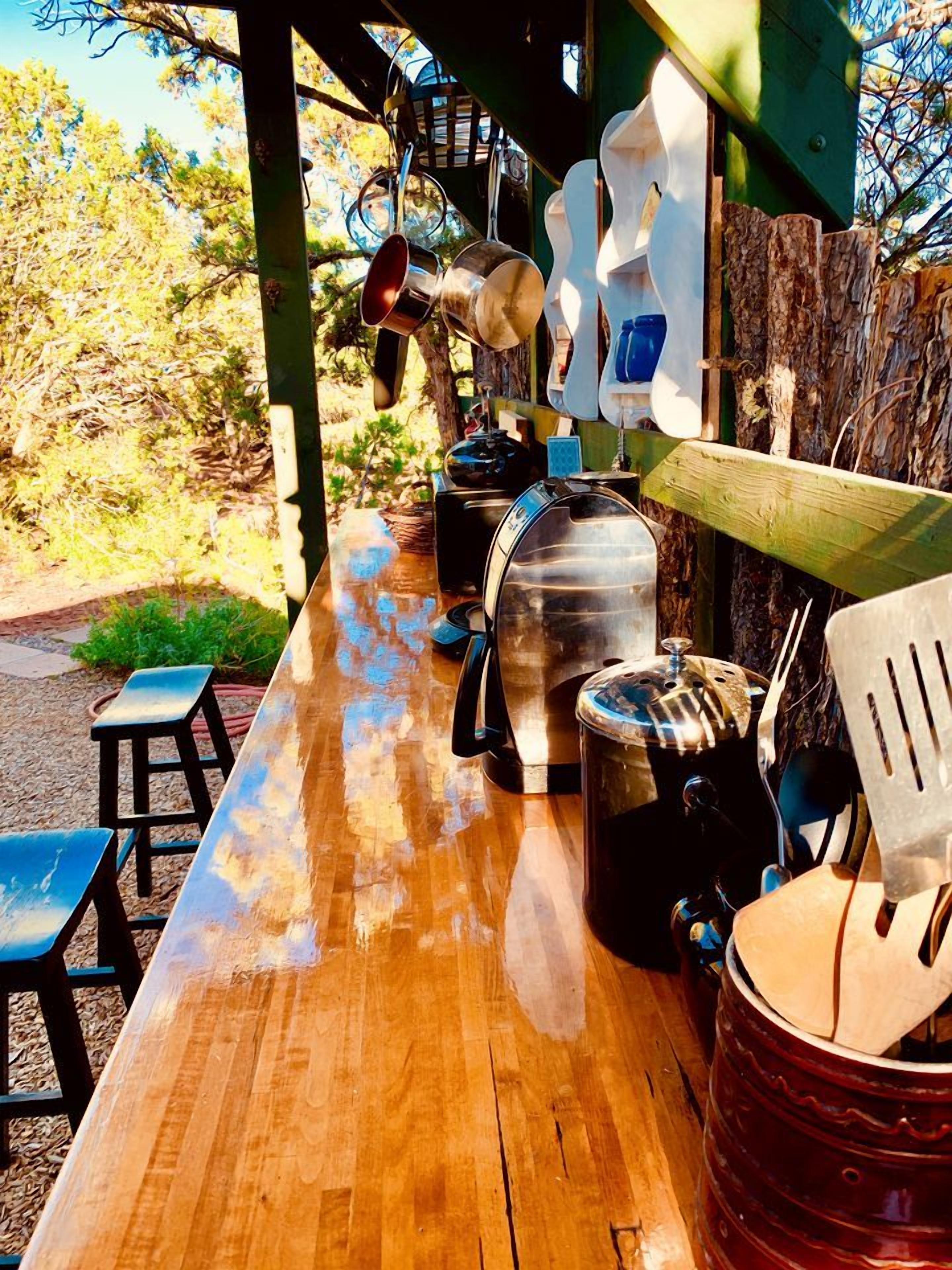 A wooden table with kitchenware and utensils, a metal pot, a blue chair, and a wooden fence in the background.