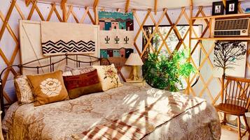 Um quarto em estilo de tenda, aconchegante e bem iluminado, com uma cama, almofadas, uma luminária e uma planta.