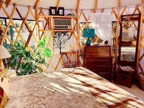 Une pièce confortable, de style tente, bien éclairée, avec un lit, des meubles en bois et une grande plante.