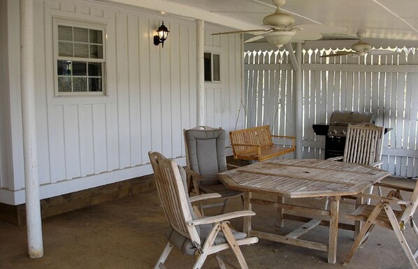 A covered patio with a wooden table and chairs, a swing, a grill, and a ceiling fan.