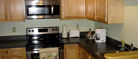 A kitchen with wooden cabinets, a stainless steel microwave, a black stove, a toaster, and a coffee maker.
