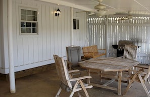 A covered patio with a wooden table and chairs, a swing, a grill, and a ceiling fan.