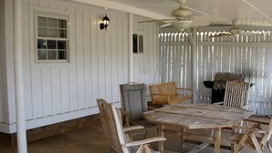 A covered patio with a wooden table and chairs, a swing, a grill, and a ceiling fan. - Pre-Civil War Servants' Cottage on Huge Horse and Cattle Farm near Charlottesville, Virginia (Gordonsville)