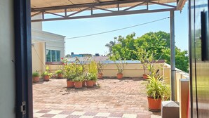 A covered outdoor area with a checkered floor, potted plants, and a view of a building in the background. - Park Inn Beach Resort (Chennai)