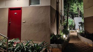 A building with a red door, a staircase leading to an upper level, and potted plants along the pathway. - Park Inn Beach Resort (Chennai)