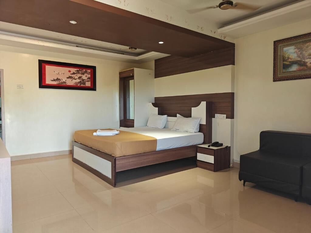 A bedroom with a bed, bedside tables, a nightstand, a black sofa, and artwork on the walls.