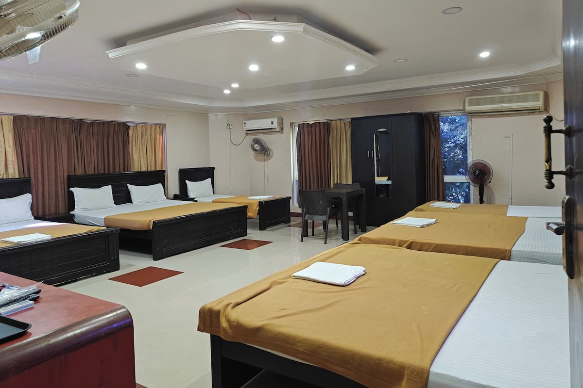 A hotel room with two beds, a desk, a chair, a wardrobe, and an air conditioning unit.