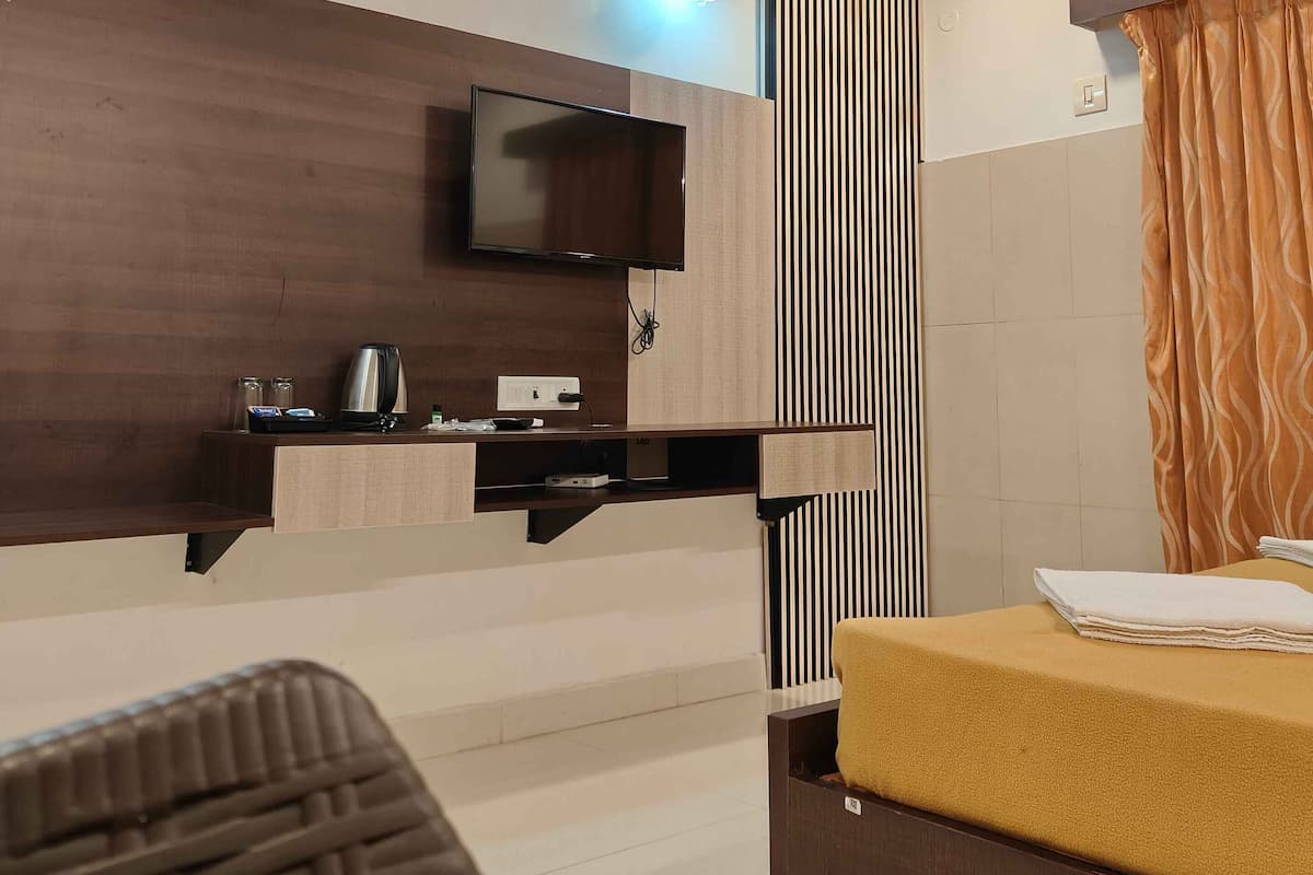 A modern hotel room with a wooden ceiling, a flat-screen TV, a small desk with a kettle, a bed with a yellow mattress, and a striped curtain.