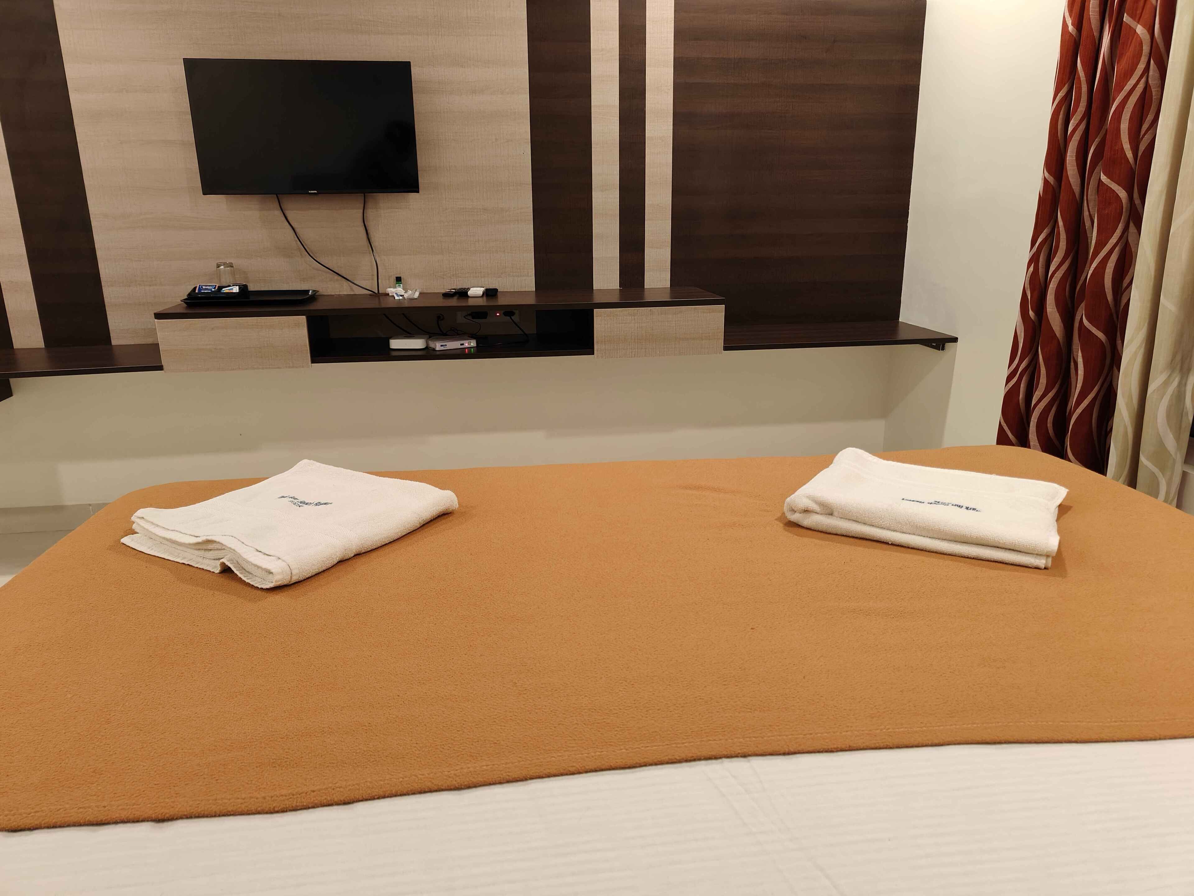 A hotel room with a bed, a flat-screen TV mounted on the wall, a small table with a bottle, and a power strip.