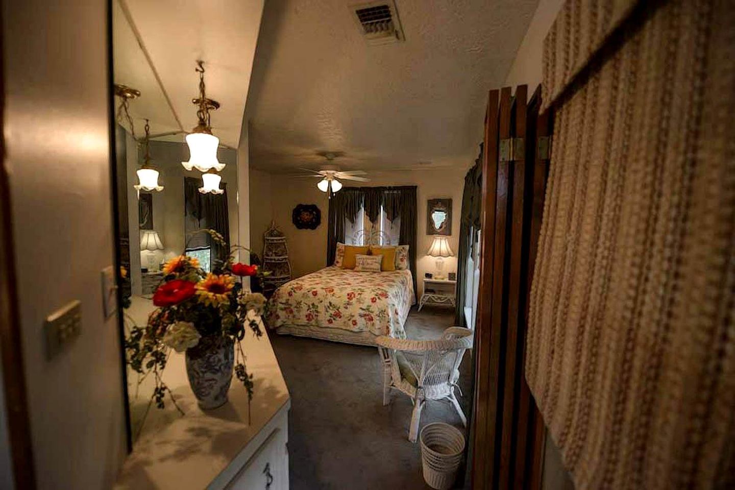 Un dormitorio con cama, mesitas de noche, un espejo y un florero con flores.