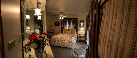 Un dormitorio con cama, mesitas de noche, un espejo y un florero con flores.