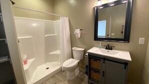 Un baño con ducha, inodoro, lavamanos y espejo.