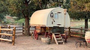 Un chariot couvert avec une échelle, un banc en bois et une clôture en bois, le tout dans un cadre naturel.