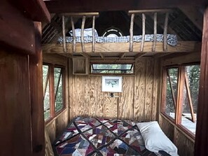 Interior de una cabaña de madera con cama, ventanas y colcha.