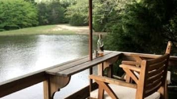 A wooden deck with a thatched umbrella, a wooden chair, and a view of a body of water.