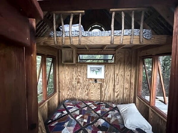 Interior de uma cabana de madeira com uma cama, janelas e um edredom.