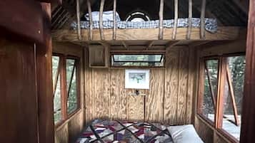 A wooden cabin interior with a bed, windows, and a quilt.