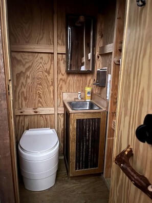 Un baño pequeño de madera con inodoro blanco, un lavamanos con espejo y un armario de madera.